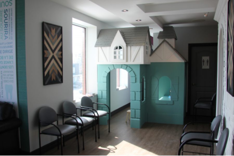 Le coin des enfants dans la salle d’attente : une maisonnette de jeu bleu-vert, près de la fenêtre et des chaises.