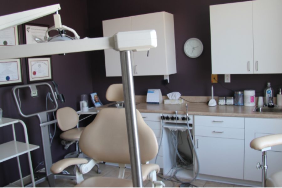 Une salle de soins au mur violet, avec le fauteuil, la lampe et les diplômes encadrés.