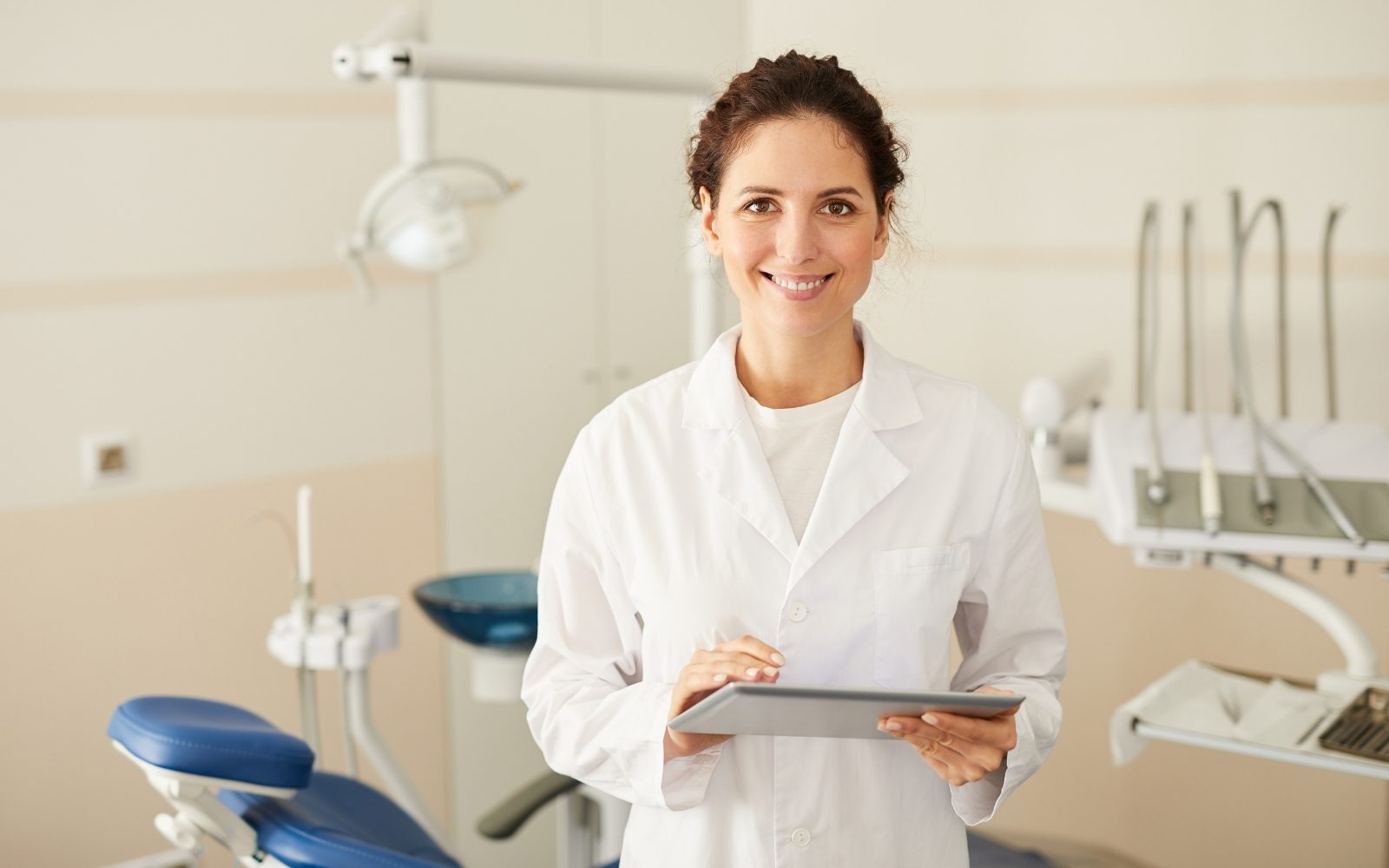 Une professionnelle en sarrau, tablette à la main, dans une salle de soins.